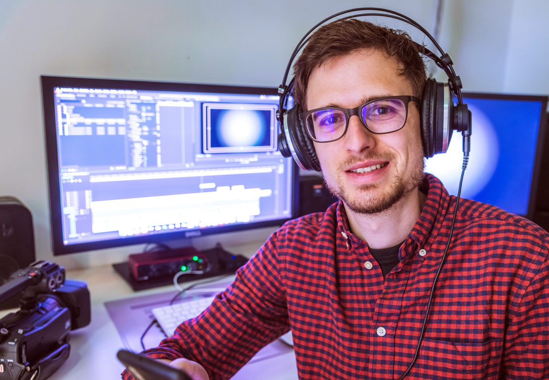 Close up of young Caucasian video editor in cutting room, monitors and the background