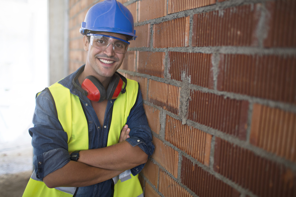 Portrait of a bricklayer leaning on a brick wall at the construction site.