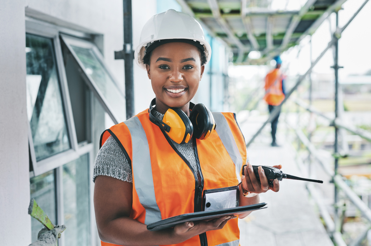 Portrait of a young woman using a digital tablet and walkie talkie while working at a construction site