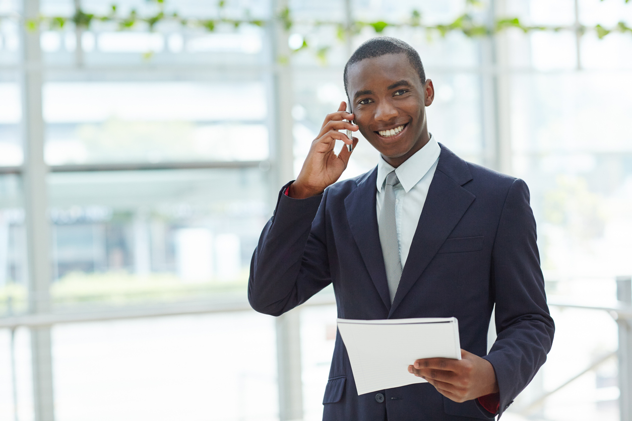 Shot of a businessman standing in a lobby talking on his phone while holding paperwork